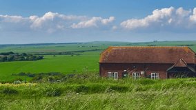 Charming cottage with a rustic roof set amidst the rolling green fields of Eastbourne, East Sussex, United Kingdom. The bright blue sky and fluffy clouds enhance the idyllic countryside setting - Powered by Shutterstock - Get 15% off with code: PIKWIZARD15