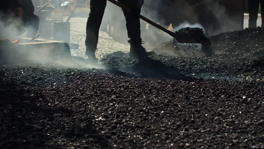 Worker shoveling hot asphalt on construction site