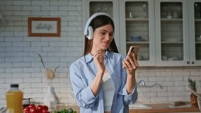Lady using smartphone kitchen reading message while cooking closeup. Joyful woman in headphones listening music turning song at cellphone. Smiling girl in earphones enjoying culinary with mobile phone - Powered by Shutterstock - Get 15% off with code: PIKWIZARD15