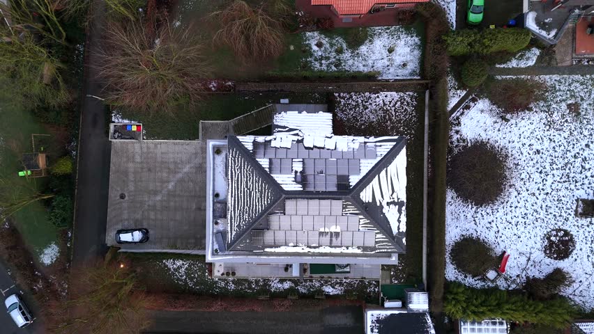 Snow-covered solar panels on roof of urban villa building. Snowy winter day in american suburb. Aerial top down rising shot. Winter snow in garden.