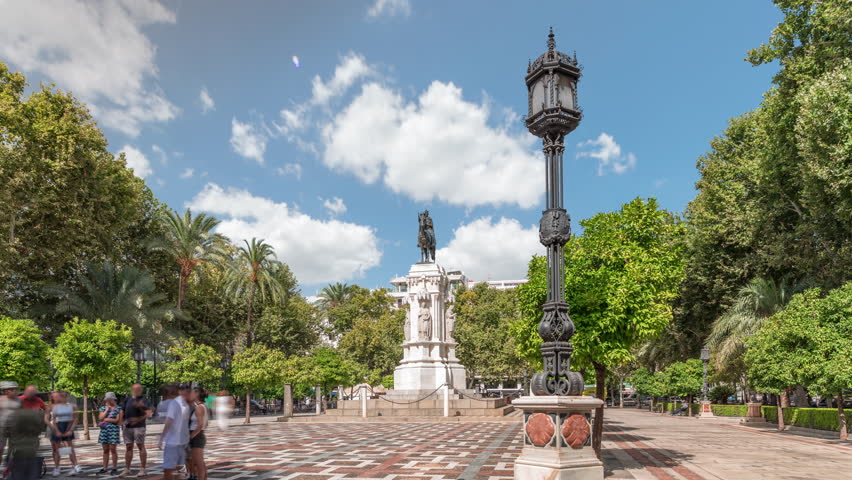 Plaza Nueva in Seville features the equestrian statue of King San Fernando, surrounded by green trees and historic buildings timelapse hyperlapse. A scenic urban space under a blue sky