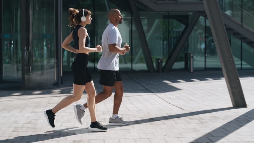 Video of athletic couple running while listening music with headphones through the city