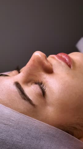 Cleansing the skin of a woman's face, female spa treatment relaxing and caring in beautician, close-up, vertical