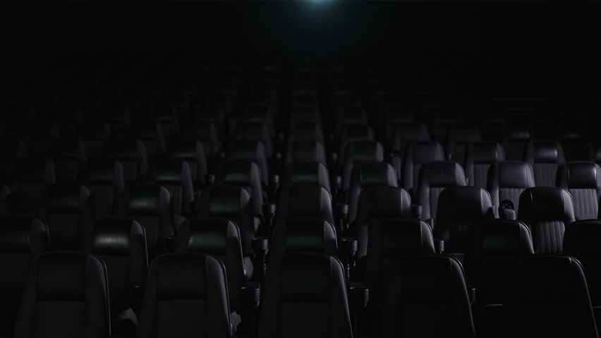 A spacious and darkened cinema hall showcasing rows of empty seats surrounded by a soft, dim projection light