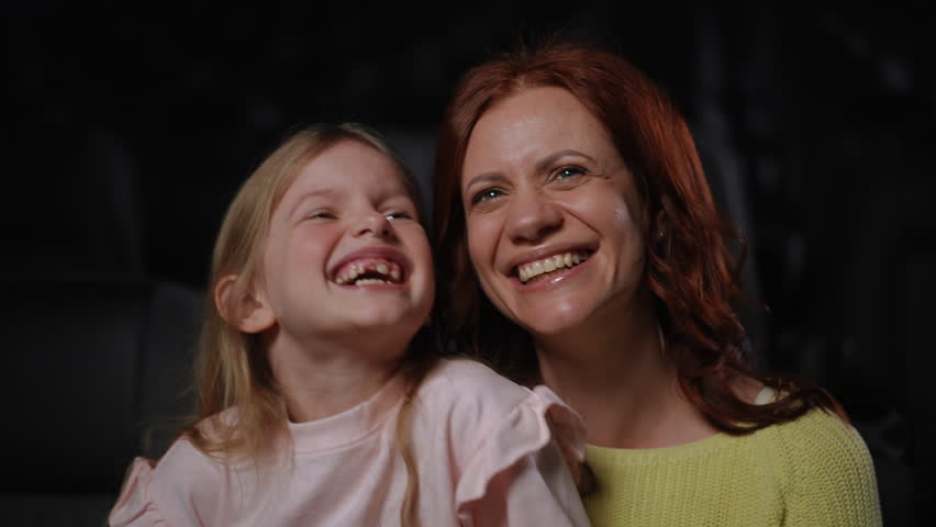 A mother and her daughter joyfully share a cinematic experience, filled with smiles and popcorn, creating memories