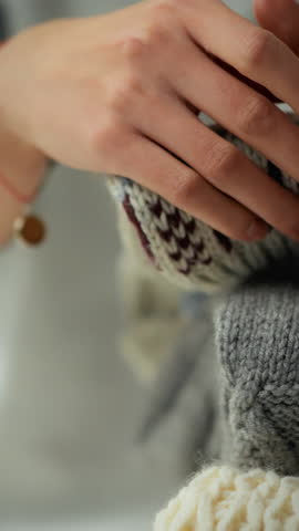 An active housewife tidies up freshly washed clothes by folding warm winter sweaters in her dressing room at home. She runs her hand over the delicate, chunky knit