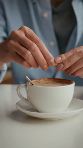 Hands gently sprinkle sweetener over a steaming cup of coffee at a cozy cafe. Enjoy the flavorful ritual as the rich aroma fills the air, enhancing the experience