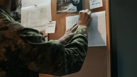 Low angle shot of young military officer in camouflage uniform examining documents, photos and maps when doing strategic planning on bulletin board - Powered by Shutterstock - Get 15% off with code: PIKWIZARD15