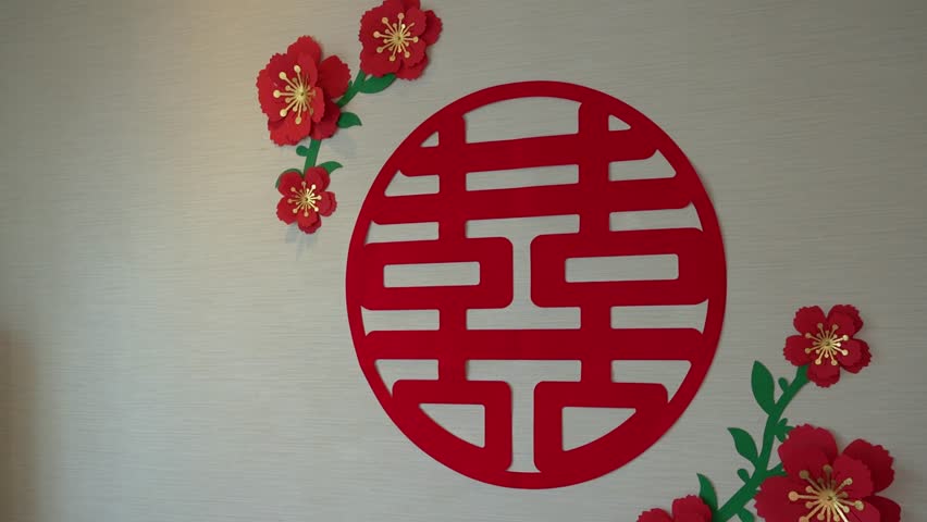 Red double happiness chinese character and paper flowers wedding decoration hanging on a white wall