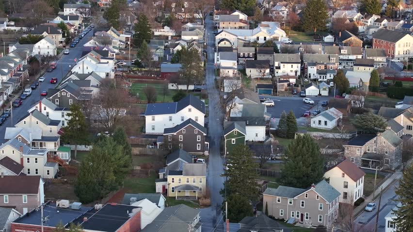 Quiet and quaint american neighborhood during sunset time in winter. Parking cars on main street. Aerial lateral wide shot. Houses and homes of Lititz, Pennsylvania.