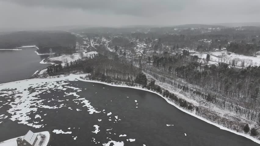 Frozen Water of Wachusett Reservoir during cold winter day in Massachusetts. Aerial orbit wide shot. Snowy winter landscape with leafless trees in Boylston.