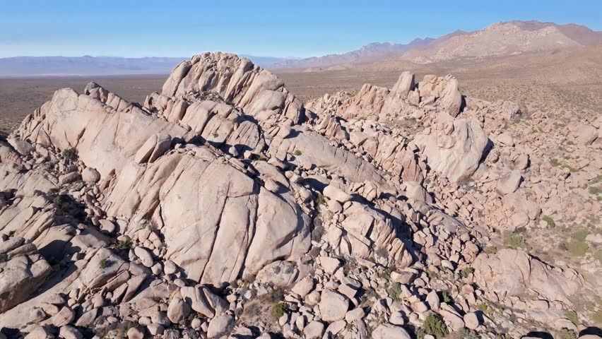 Rugged hill rock formation Kelso Pinto Basin Dunes Joshua Tree National Park California aerial drone Yucca Trees San Fernando County Mojave Colorado desert blue sky sunny afternoon forward motion