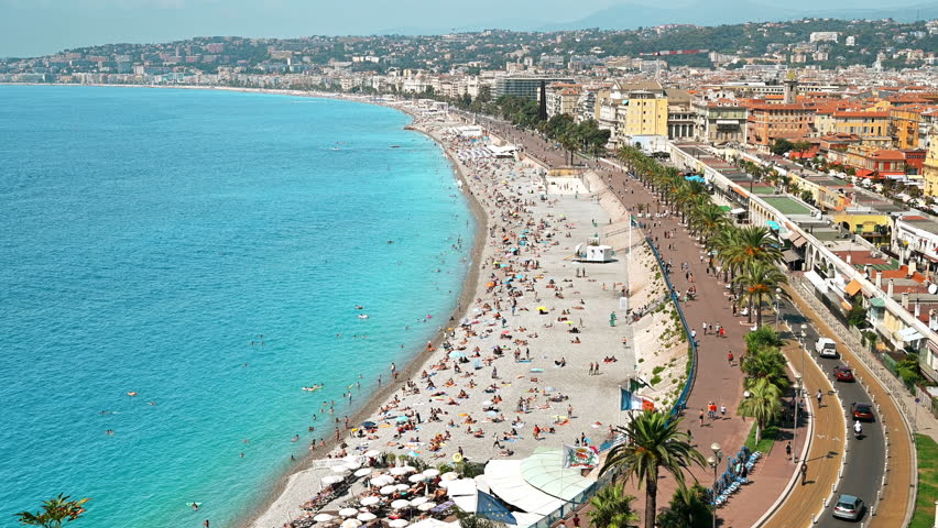 View of the cote d'Azur in Nice, France. Multiple resting on the beach people, buildings, blue water of the Mediterranean sea