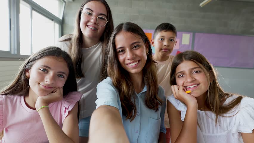 Small group of primary school children taking selfie portrait or doing video call with phone in classroom. Elementary education concept. They look at the camera. Teenager people, teens.