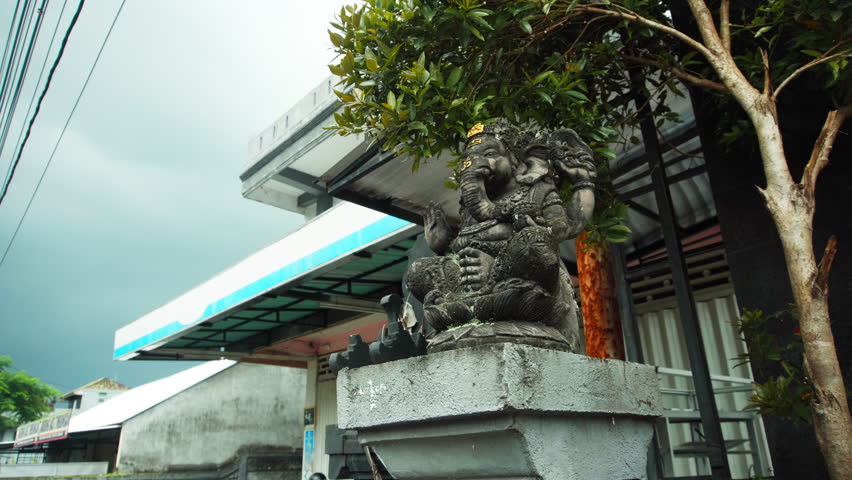 An old stone statue of Ganesha covered with a moss standing on the street 