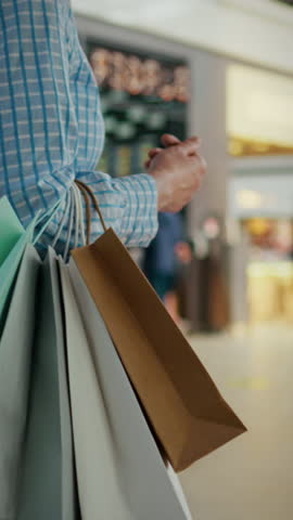 In a busy shopping mall, a man carries several bags filled with purchases. A young modern girl in a shopping mall carries bags with purchases of clothes in a good mood and with a confident gait