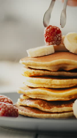 This delightful stack of golden pancakes is beautifully garnished with ripe banana slices and juicy raspberries. Perfect for a satisfying breakfast or brunch, a true treat for any morning