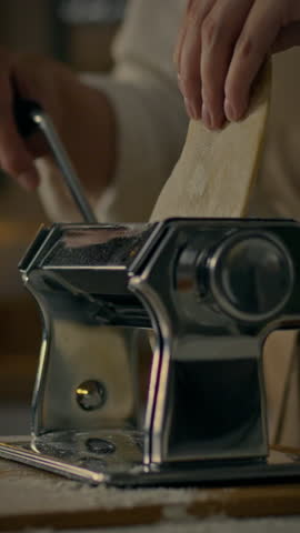 A person skillfully uses a manual pasta maker to roll out fresh dough in a warm kitchen