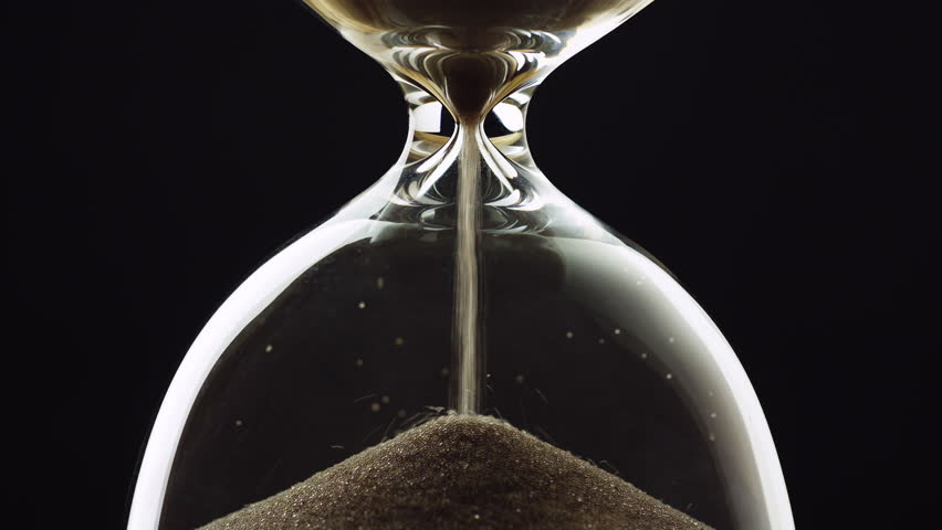 Sand running out in an hourglass, golden sand grains flowing through the glass device, timelapse shot. Time, and urgency concept.