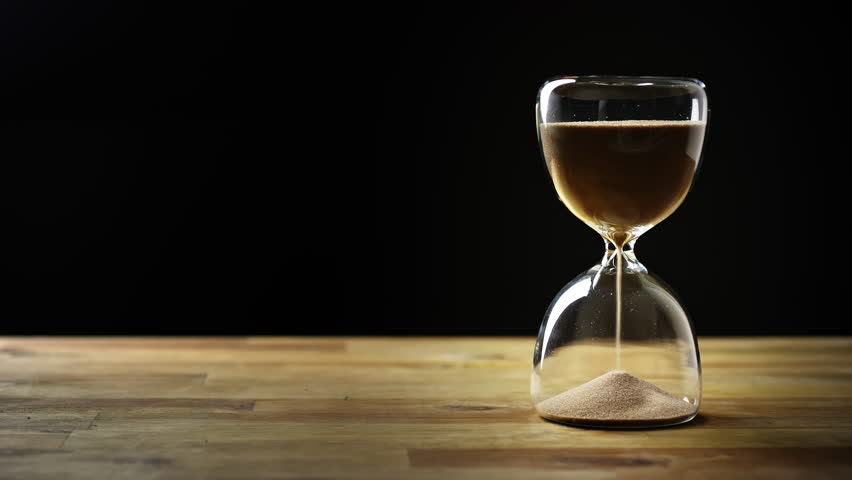 Sand flowing in an hourglass on a wooden table and with a black background, timelapse shot. Time running out concept.