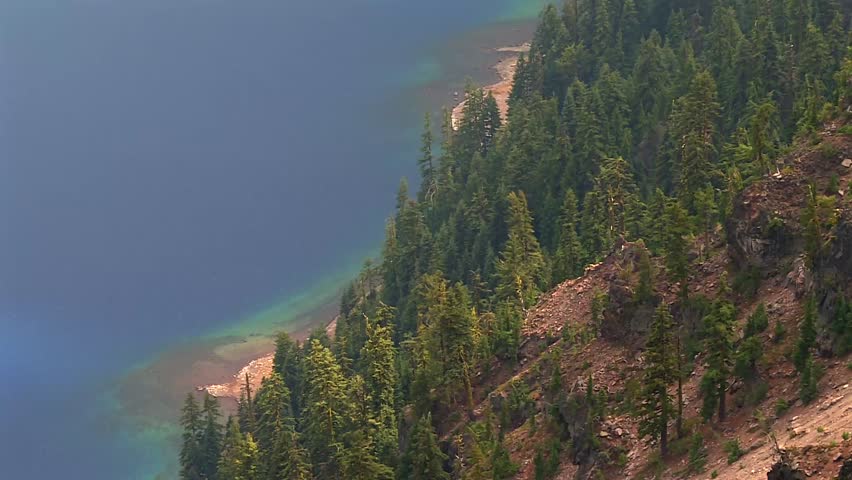 Steep ridge with evergreen pines and turquoise waters at Crater Lake shores. Crater lake volcanic, caldera lake in Oregon, USA