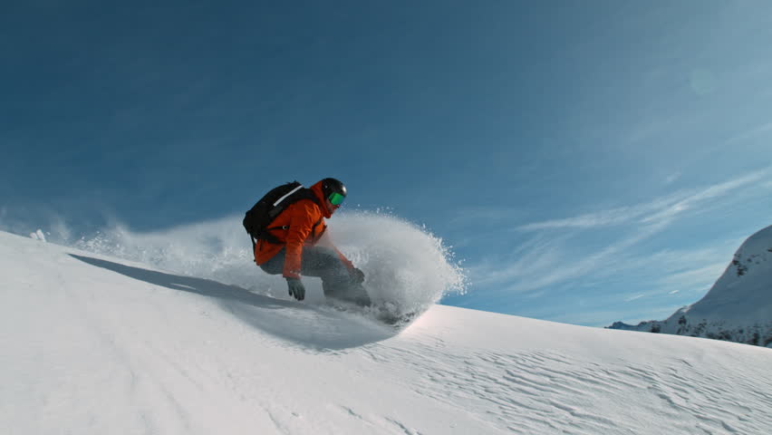 Snowboard rider riding down fresh powder during sunny day, Alpine scenery. Super slow motion at 1000 fps.