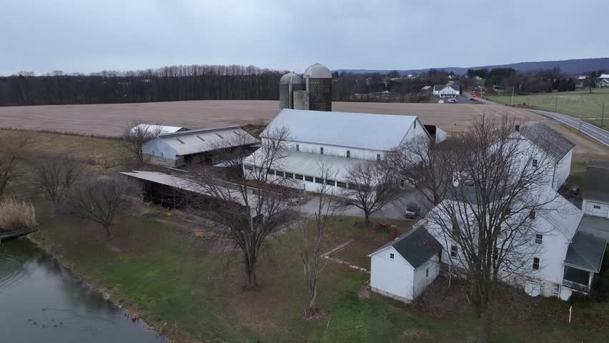 Rustic farmhouse with traditional barn and frozen lake in winter.American countryside in rural area.Aerial top down rise shot. Charming homestead in classical midwest style. Quiet rural suburb in USA