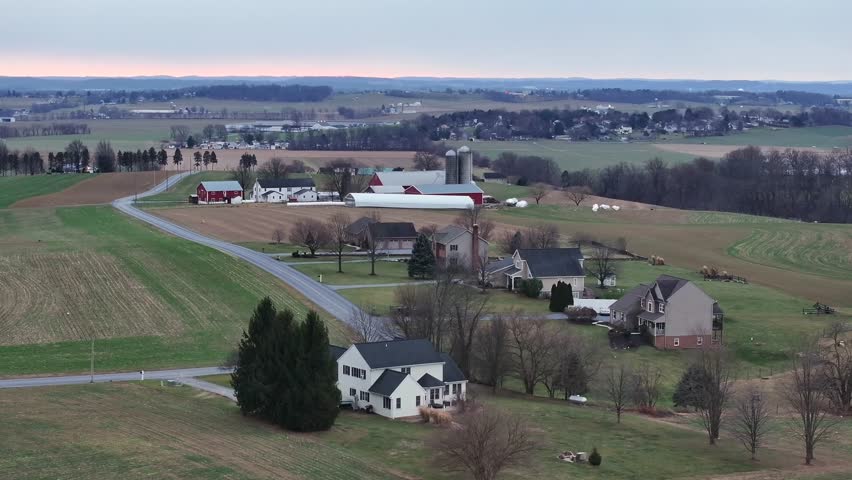 Large Farmstead with fields, single family houses and barns during early morning in winter. Pennsylvanian Countryside in rural area. Silo Storage and scenic landscape. Aerial approaching shot.