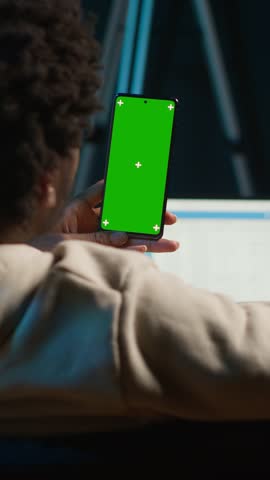 Vertical Video Confident tech user looking at isolated mockup display in his living room, relaxing with his remote job on the couch. African american happy adult browses the internet. Camera A.