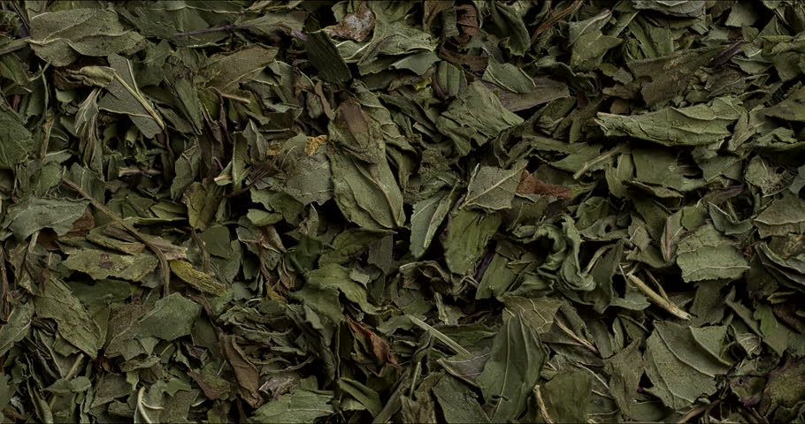 Close-up view of dried, chopped peppermint leaves as a background. Dry herb texture. Zoom in while rotating.