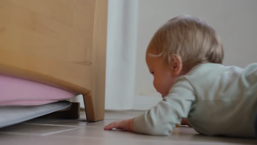 Curious and adventurous baby energetically reaches under piece of furniture, showcasing their innate curiosity and exploration as they joyfully discover their enchanting environment