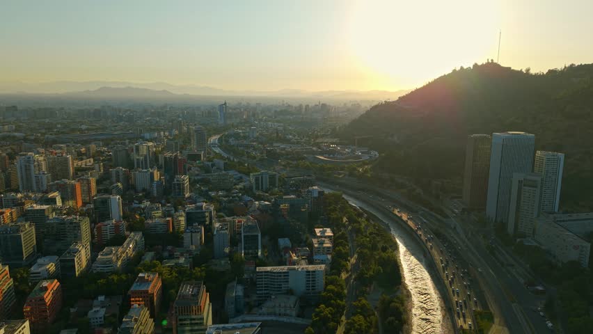Aerial establishing of Santiago buildings by Mapocho river, sunbeam peaking through hill. Chile