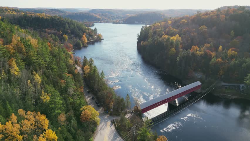 Aerial view of beautiful old red bridge and smooth green waters of a lake on a sunny autumn day. Bird