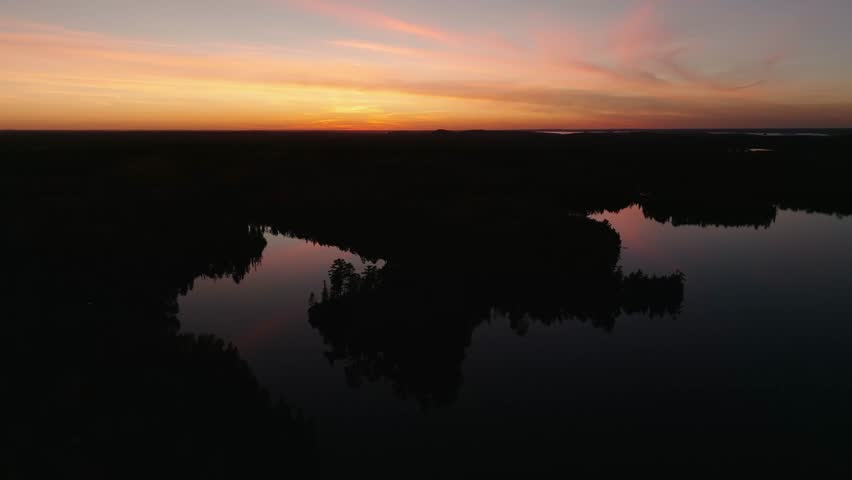 Stunning Sunset Drone Pull Back Over Calm Minnesota Lake. This lake was completely glass calm, reflecting the beautiful sunset off of the water. Captured in Ely, Minnesota. Clip available up to 60fps