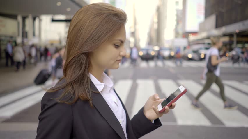 A Young Woman Uses her Smart Phone as She Walks along the City Streets