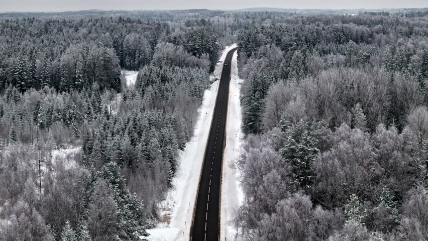 Aerial view of an asphalt road through snow-covered pine forests.