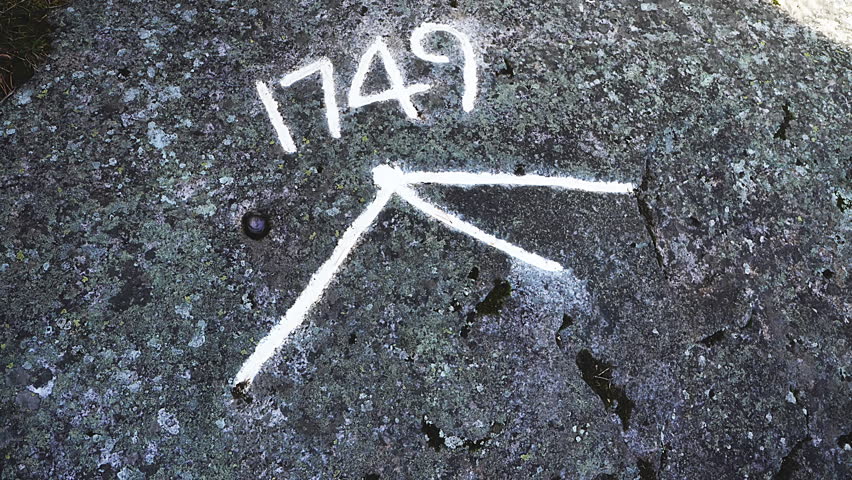 Close up of white painted markings, featuring the year 1749 and an arrow like symbol, on a dark rock surface indicating a historical water level on Ratan island, Sweden