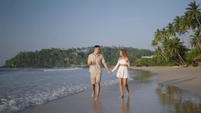 Happy couple walk, drink coconut water on ocean beach. Young woman, man hold hands, kiss. Romantic newlyweds clink cocktails, enjoy honeymoon vacation at tropical sea shore on sunrise. - Powered by Shutterstock - Get 15% off with code: PIKWIZARD15