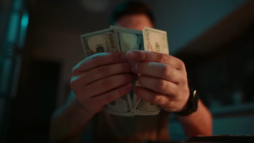 Counting cash at night in a dimly lit room while planning the next move