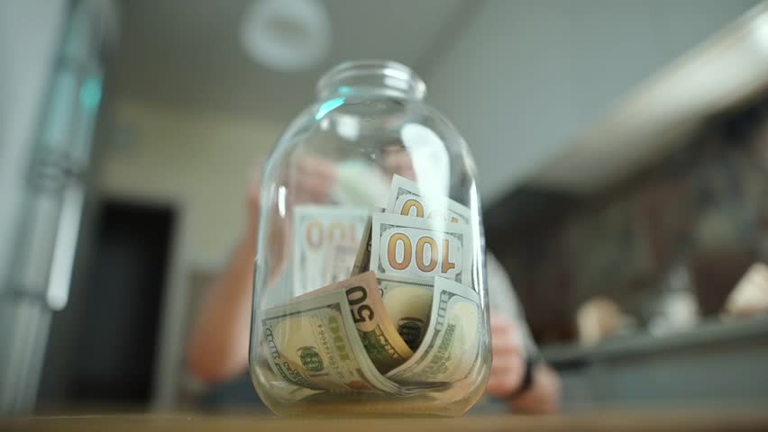Person saving money in a jar at home while planning financial goals
