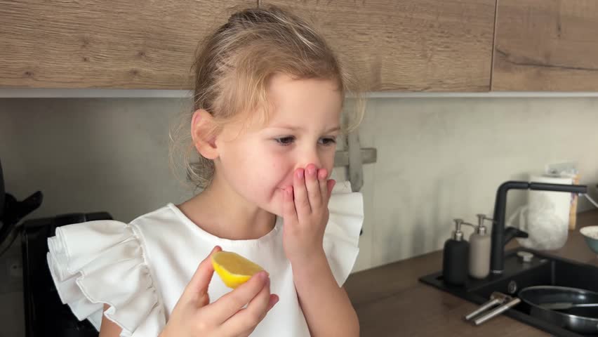 Little girl wincing as she tastes lemon sitting in kitchen. High quality 4k footage