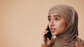A young Arab woman wearing a hijab engages in a phone conversation. She appears focused and expressive, set against a neutral studio background. - Powered by Shutterstock - Get 15% off with code: PIKWIZARD15
