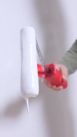 vertical video little girl painter using a paint roller, applying fresh white paint on a wall during renovation work, with paint dripping down as part of the home improvement process