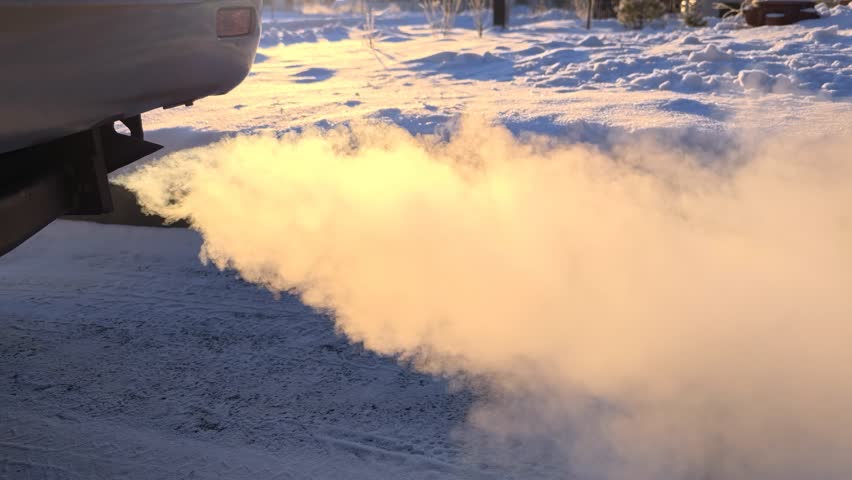 Smoke emitted from the exhaust pipe of car in winter frost. The sun illuminates the smoke with backlight. 