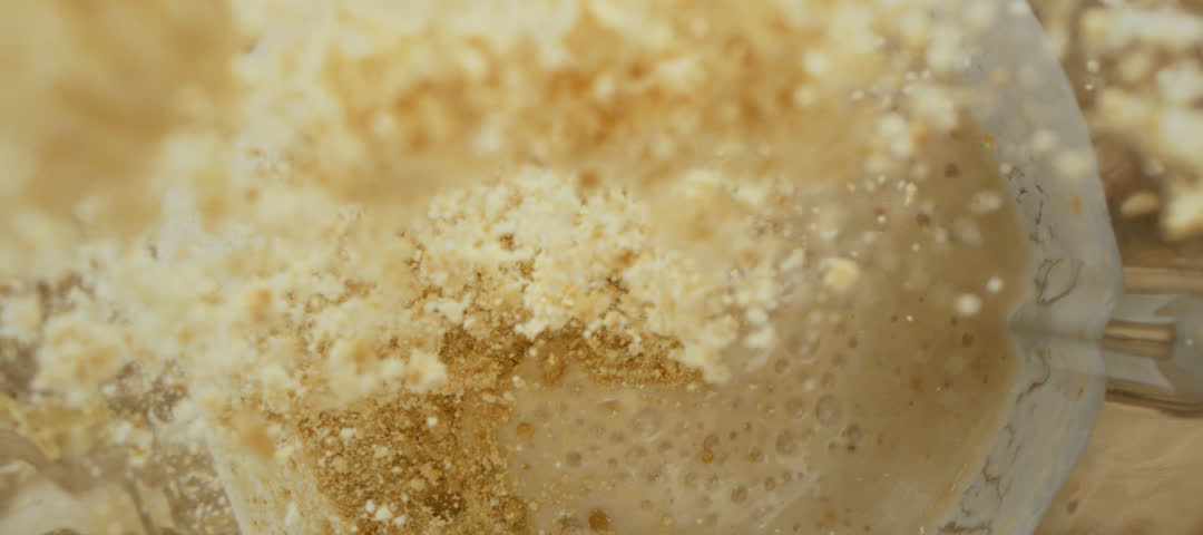 Slow-motion shot of an unrecognizable person pouring protein powder into milkshake in the blender jar