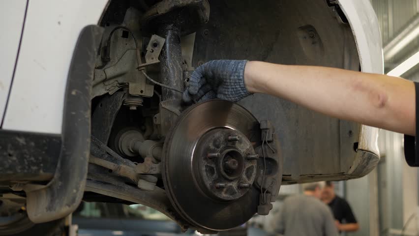 Close-up of an auto mechanic replacing brake pads on a car wheel at a service station. A mechanic repairs a car in the workshop. An auto mechanic checks the car.