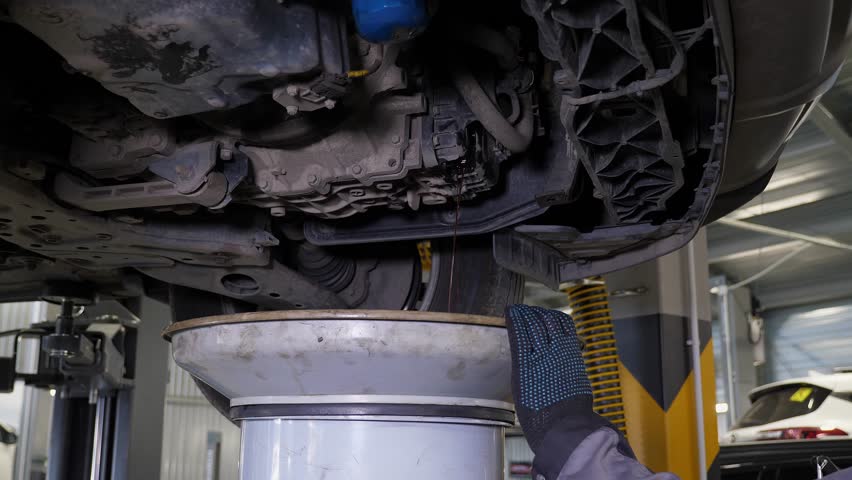 Close-up of the waste oil drain and technical inspection of the car on the lift in the garage. Car service. The mechanic changes the oil in the car.
