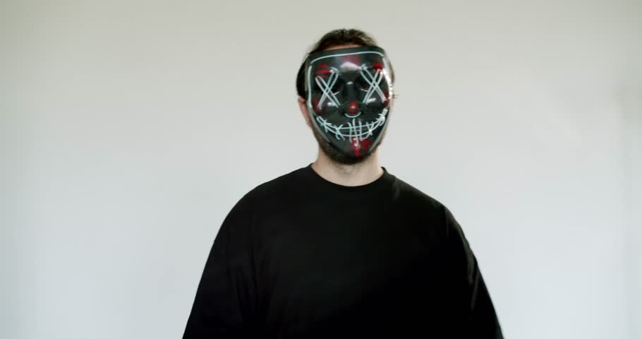 A man in a purge mask counts money. The mask has an evil smile and red X's over the eyes. He is wearing a black shirt and holding several large bills.