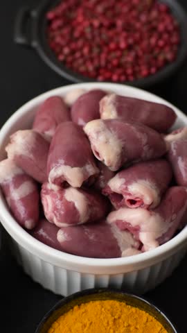 Raw chicken hearts with salt, spices and herbs on a dark concrete background