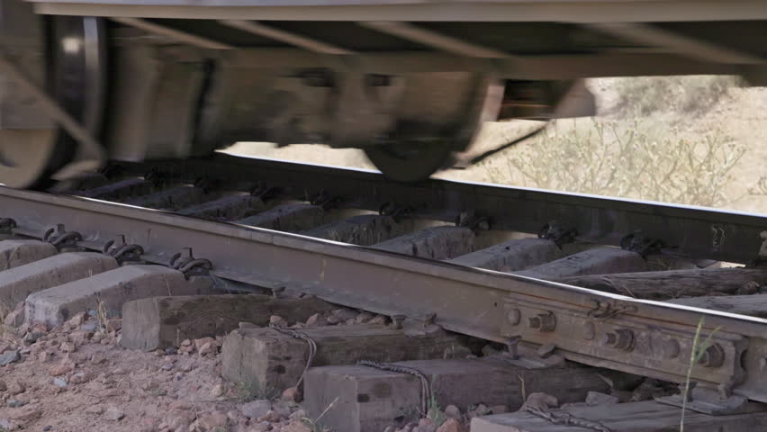 A closeup view of train wheels moving on old bending railroad tracks with old wooden sleepers section at sunny summer day